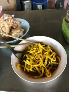 A picture of the meal with chopsticks and noodles in the back on a table in the market.