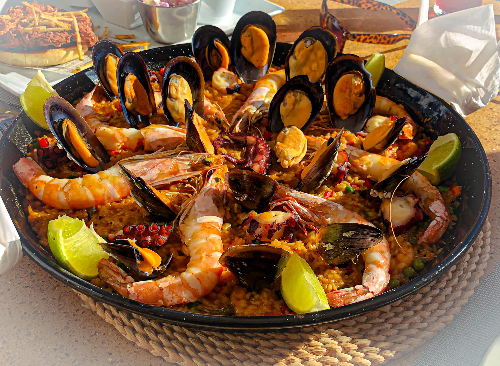 Paella Large Black Dish with prawns, mussels, rice and lemons inside. Background blurred. Marbella, Spain