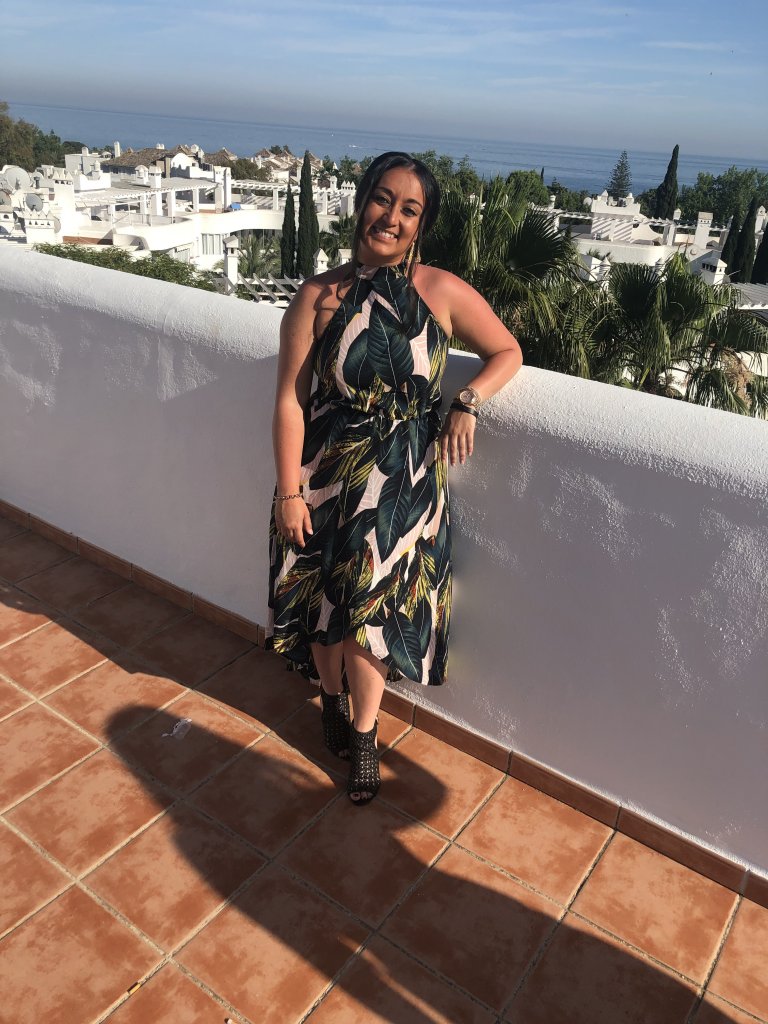 Picture of me in tropical green long dress with white wall behind me and Marbella villas in the background. Ocean in far background.