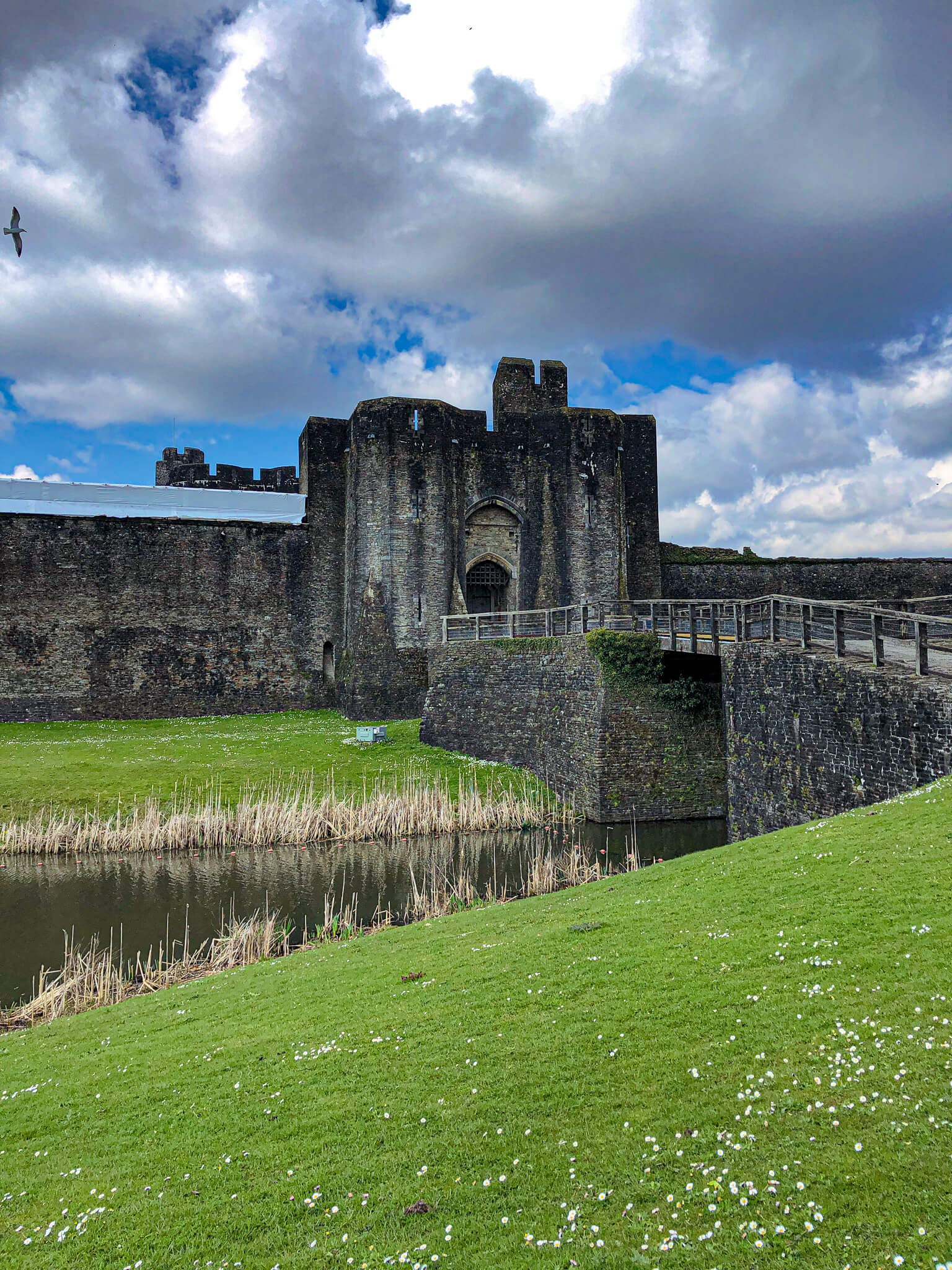 Caerphilly castle with grass in forefront, castle in centre and sky and clouds in back