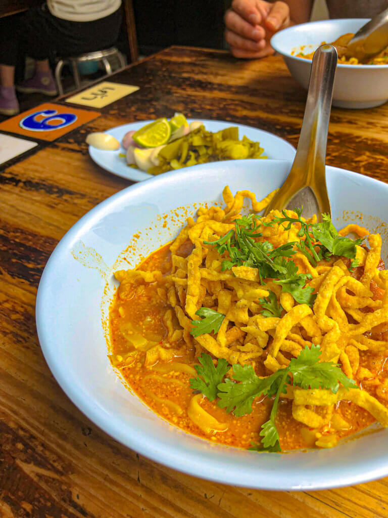 Bowl of Khao Soi in Chiang Mai on a wooden table. Street food in Southeast Asia.
