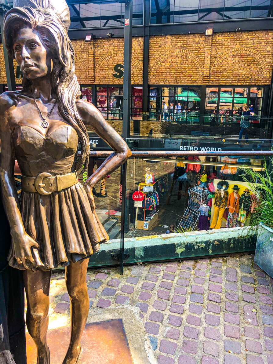 Amy Winehouse Statue Camden in centre of photo with Camden Market building in background and lower level of Stables Market Camden
