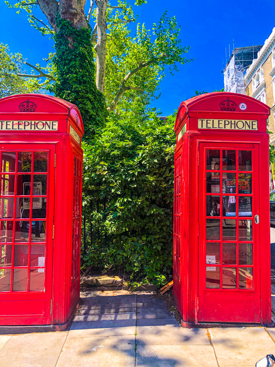 two famous London red phone boxes in centre of image with trees in background, Primrose Hill, London