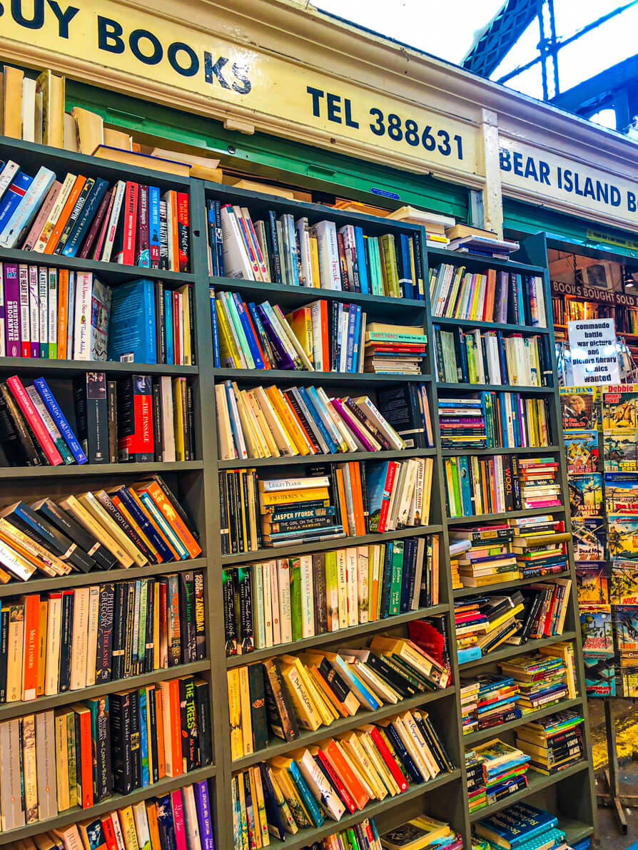 Image of the left hand side of Bear Island Book Exchange in Cardiff Market. Image shows the bookshop sign at the top and underneath shelves full to the brim of books in all shapes and balances. 