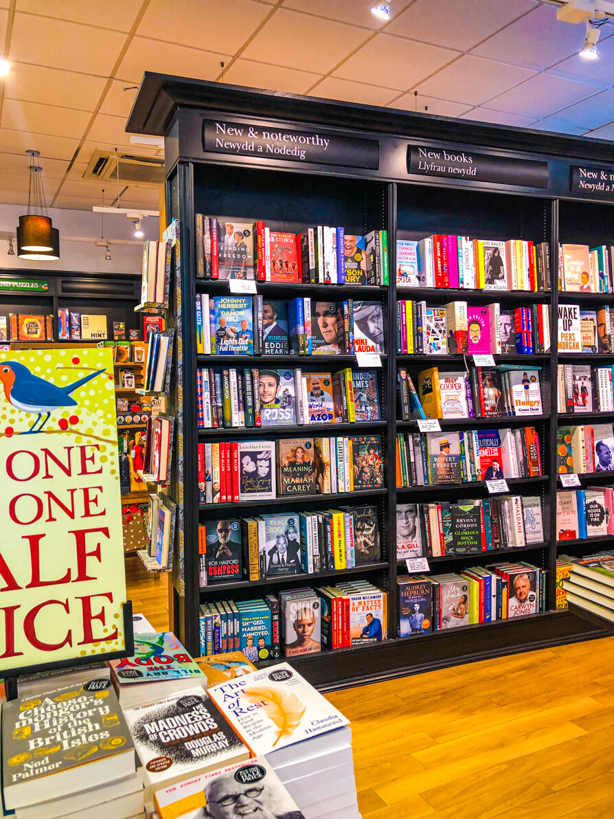 Image of Waterstones Cardiff new releases shelves to the right and 'buy one get one half price' yellow sign on a table of books to the left.