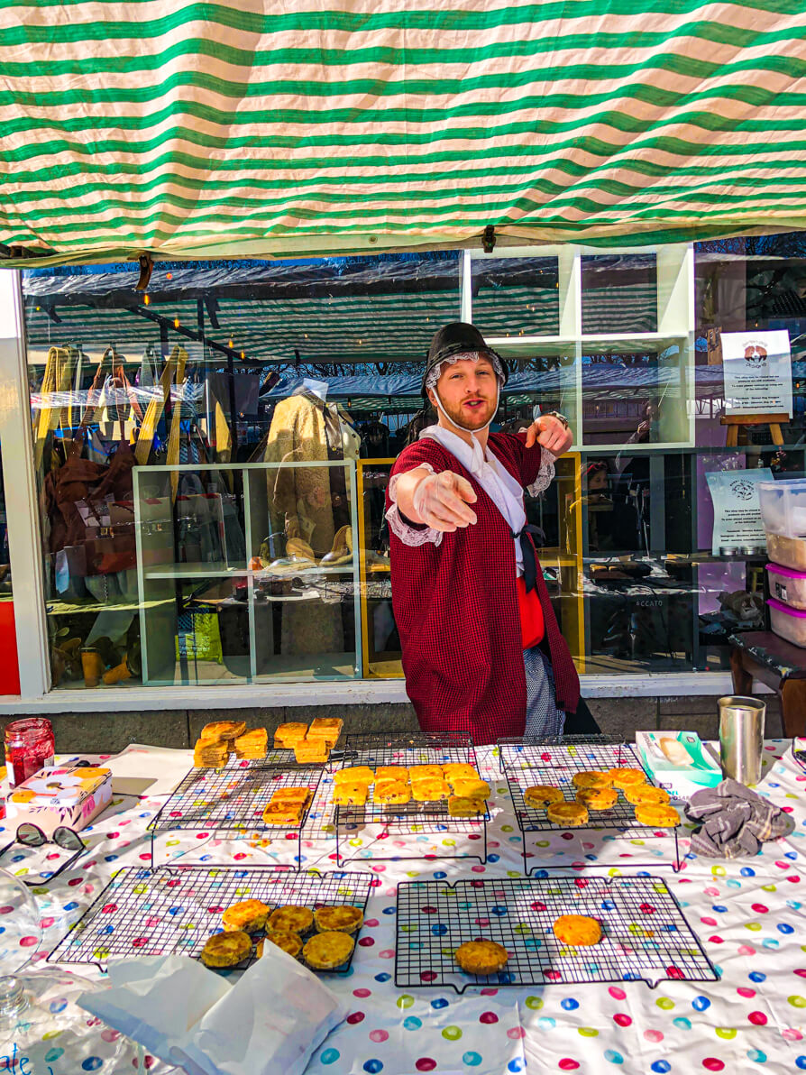 Image of owner of Rogue Welsh Cakes dressed as a traditional Welsh lady behind his stall of Welsh cakes in Cardiff