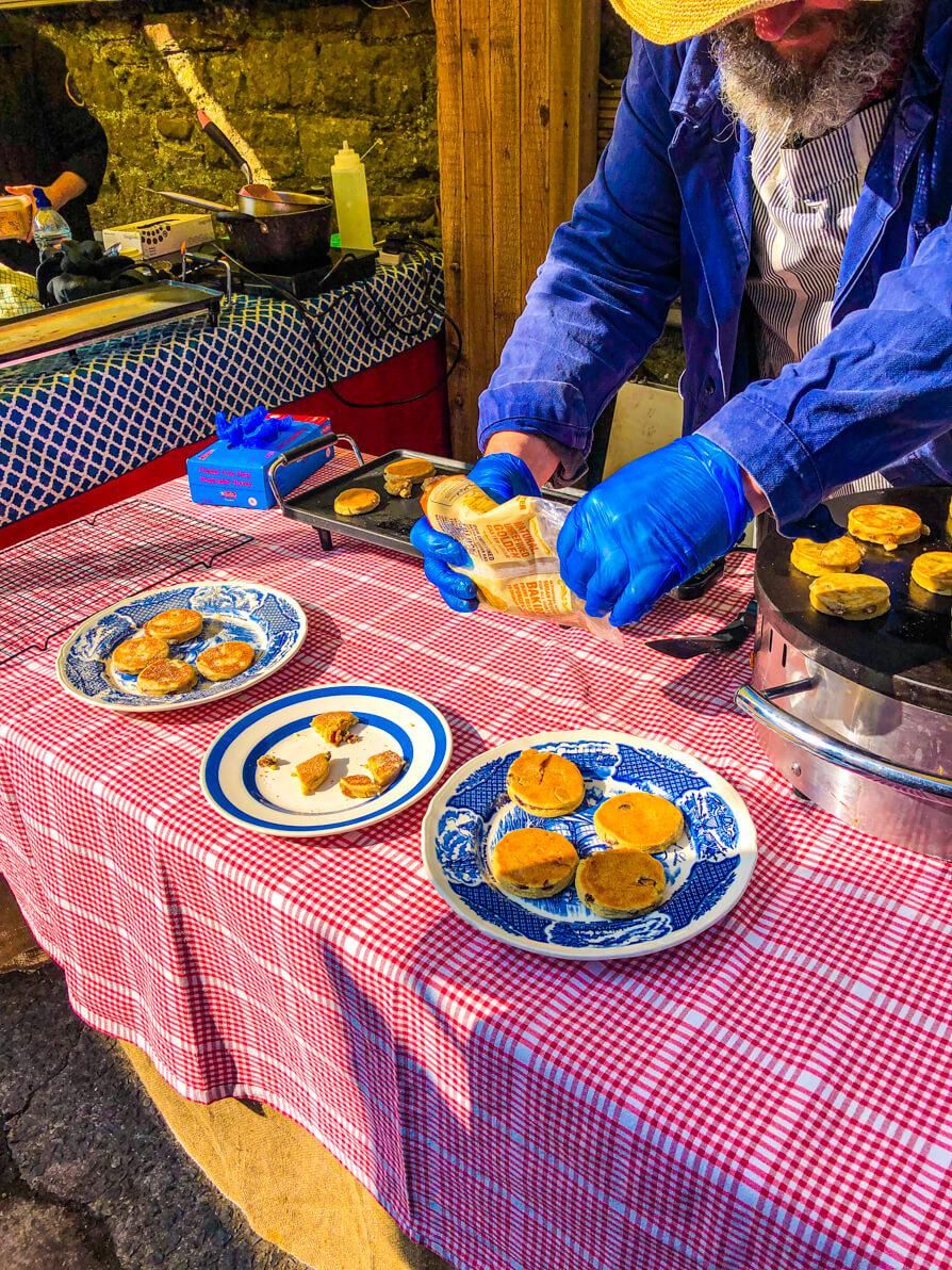 Image of Pontcanna Market Welsh cakes on blue plates on a pink table with owner sprinkling sugar on top in Cardiff
