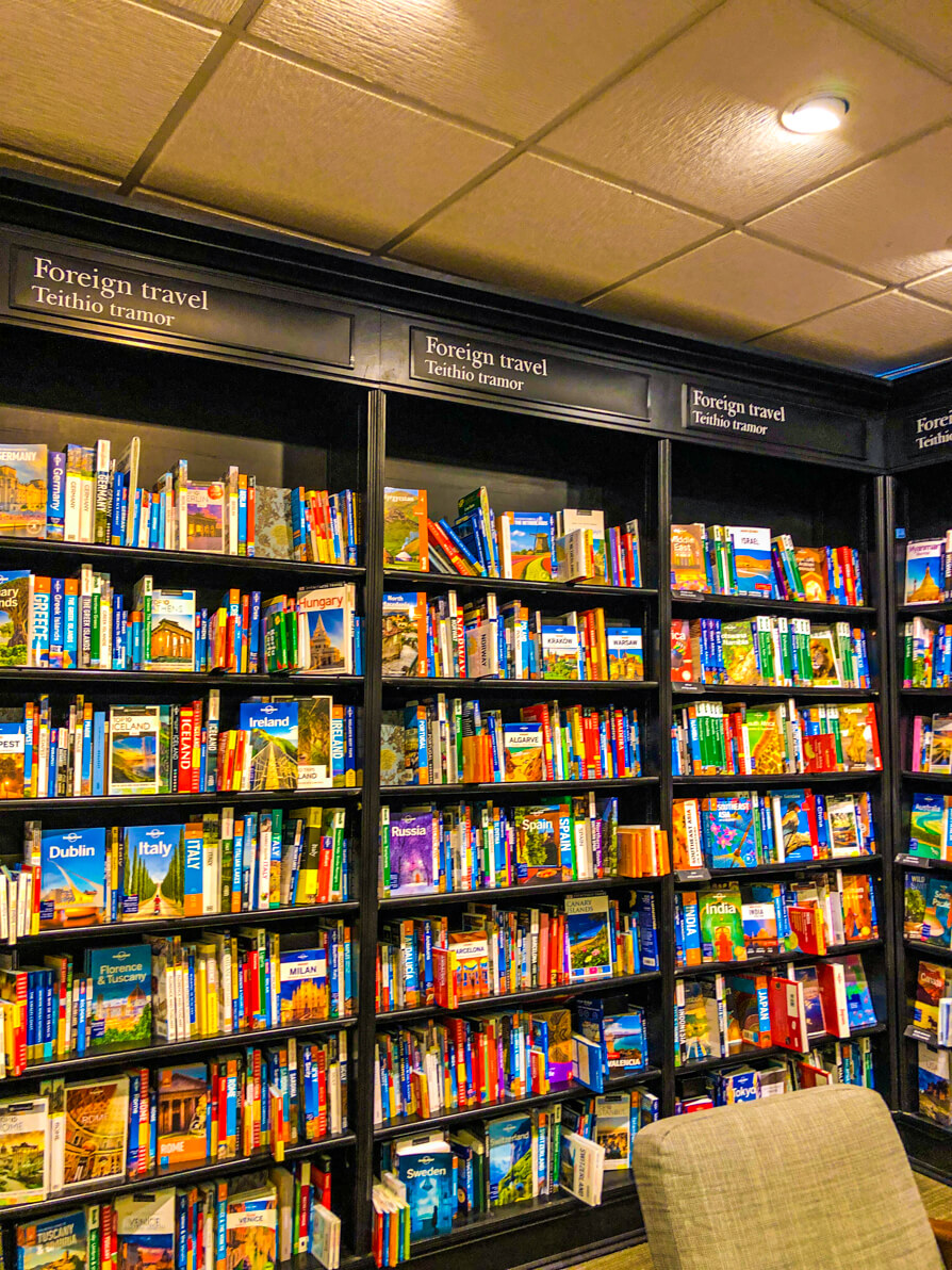 Image of three bookshelves full of travel guides in Cardiff Waterstones with beige chair in front