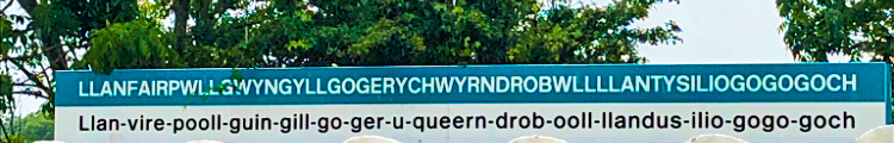 Image of train station platform with longest Welsh place name in Welsh and phonetic beneath. 