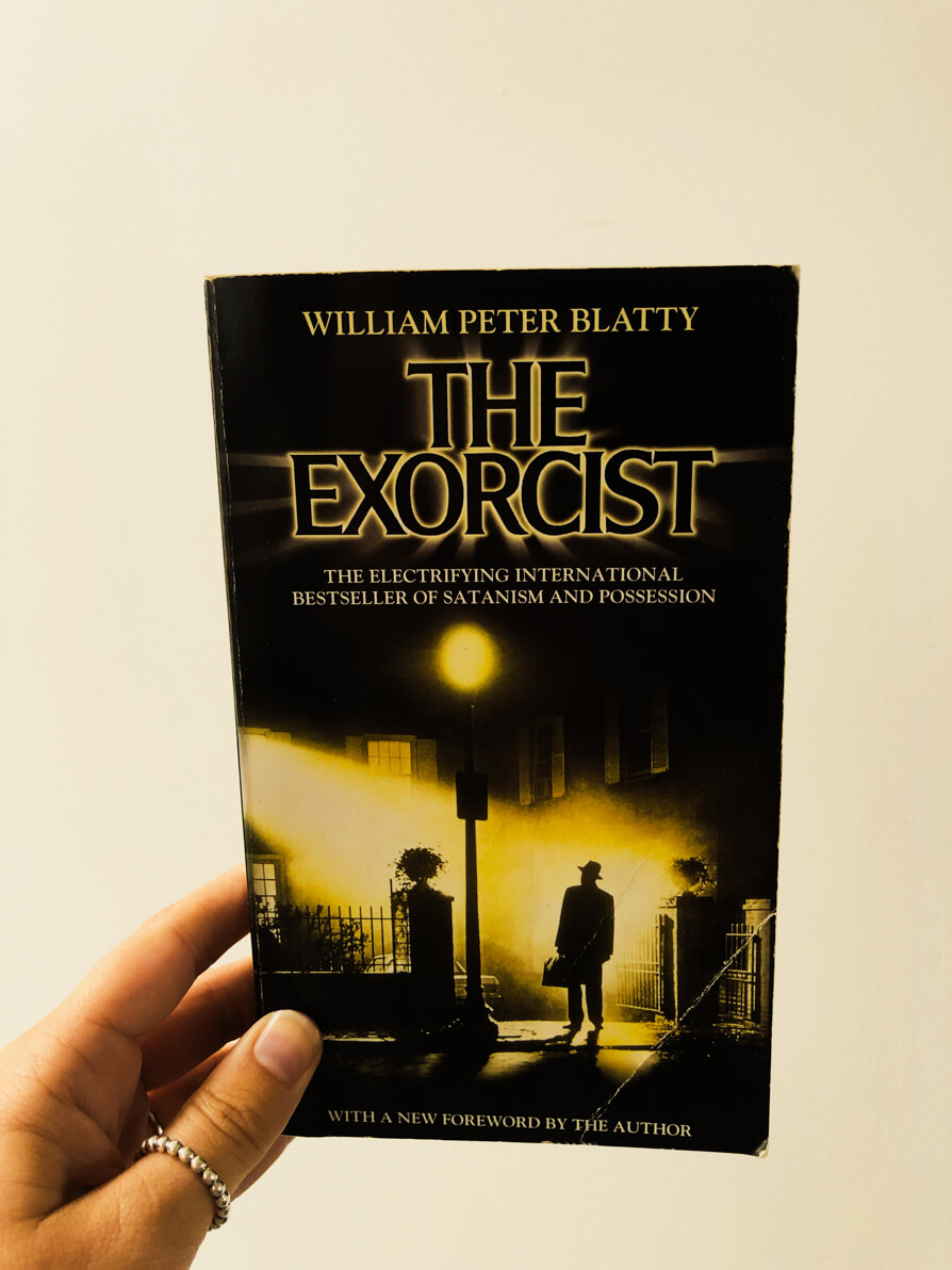 Image of Shireen's left hand holding up The Exorcist Book Cover in front of a white wall