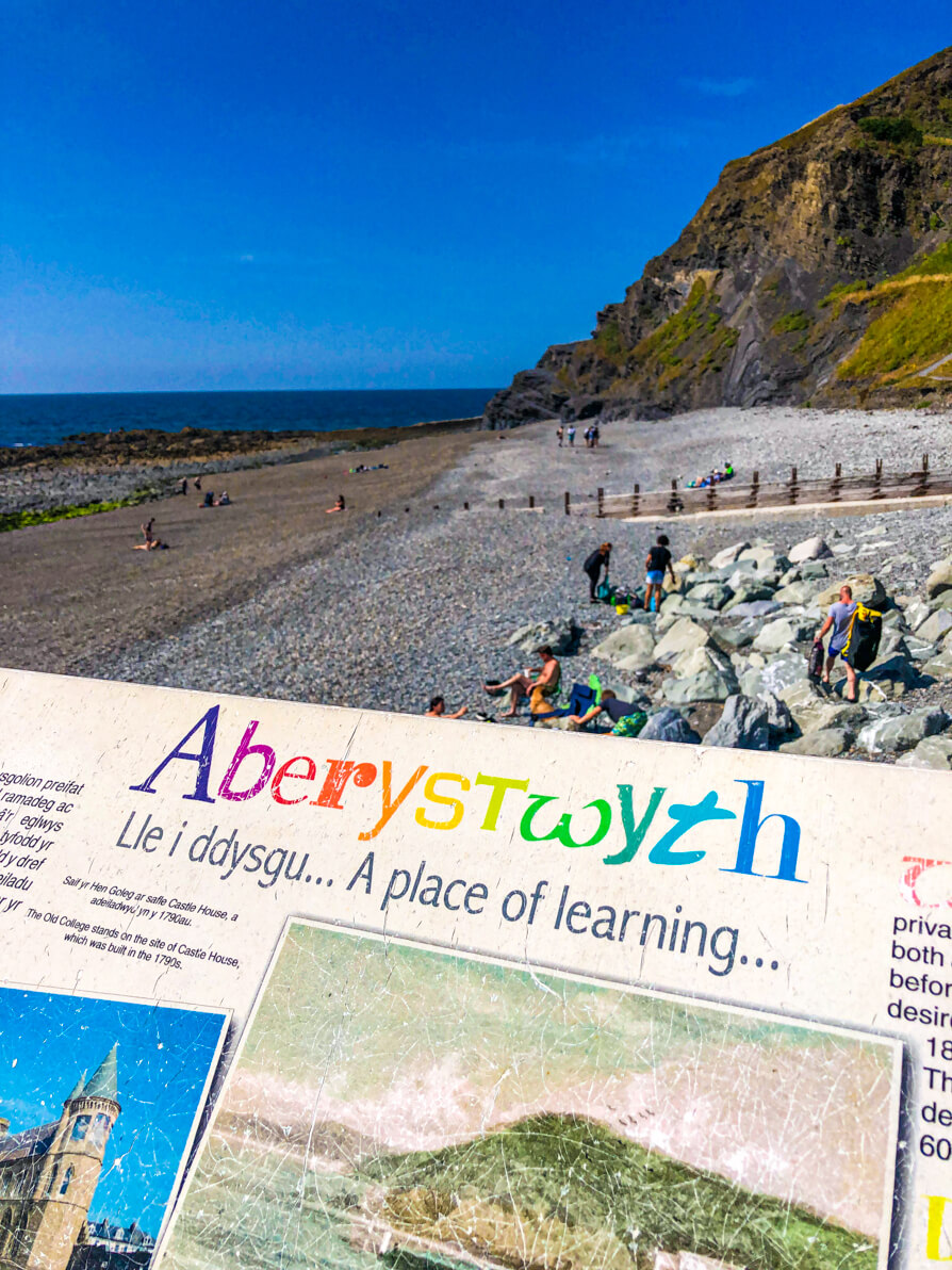 Notice board reading Aberystwyth 'a place of learning' with beach and sea in background