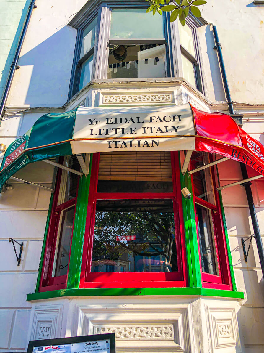 Exterior of Little Italy in Aberystwyth. Image shows the two windows with restaurant sign saying Little Italy pained white, green and red.