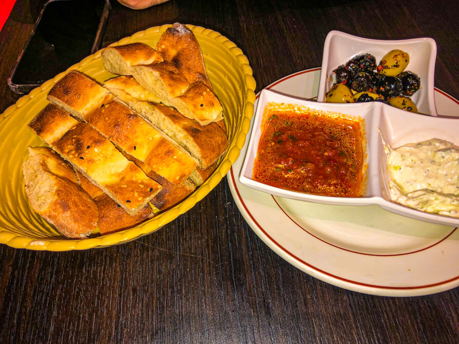 Saray restaurant starters on the house including bowl of bread and three white dishes of dips and olives