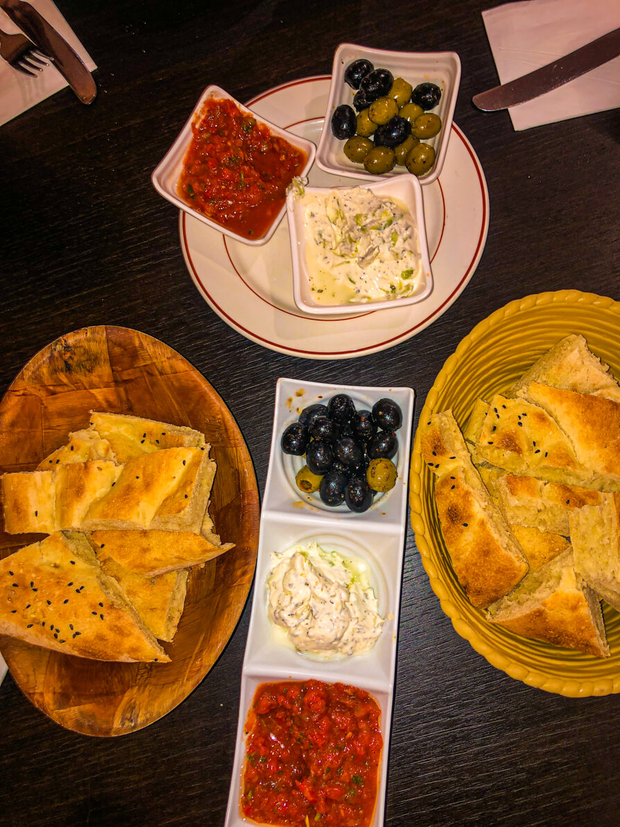 Bird's eye view of Saray free starters: two boys of bread and 6 white dishes of dips and olives