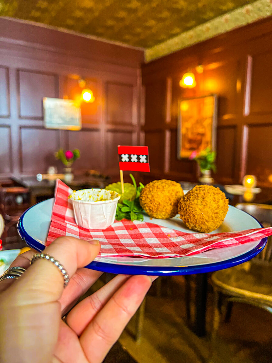 Bitterballen and pickles on a white plate and red and white napkin with Amsterdam flag on a stick in the centre on Amsterdam food tour with Eating Europe