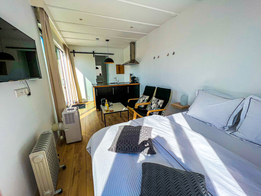 Interior of airbnb Delft shows bed, tv, two chairs, table and kitchen counter area