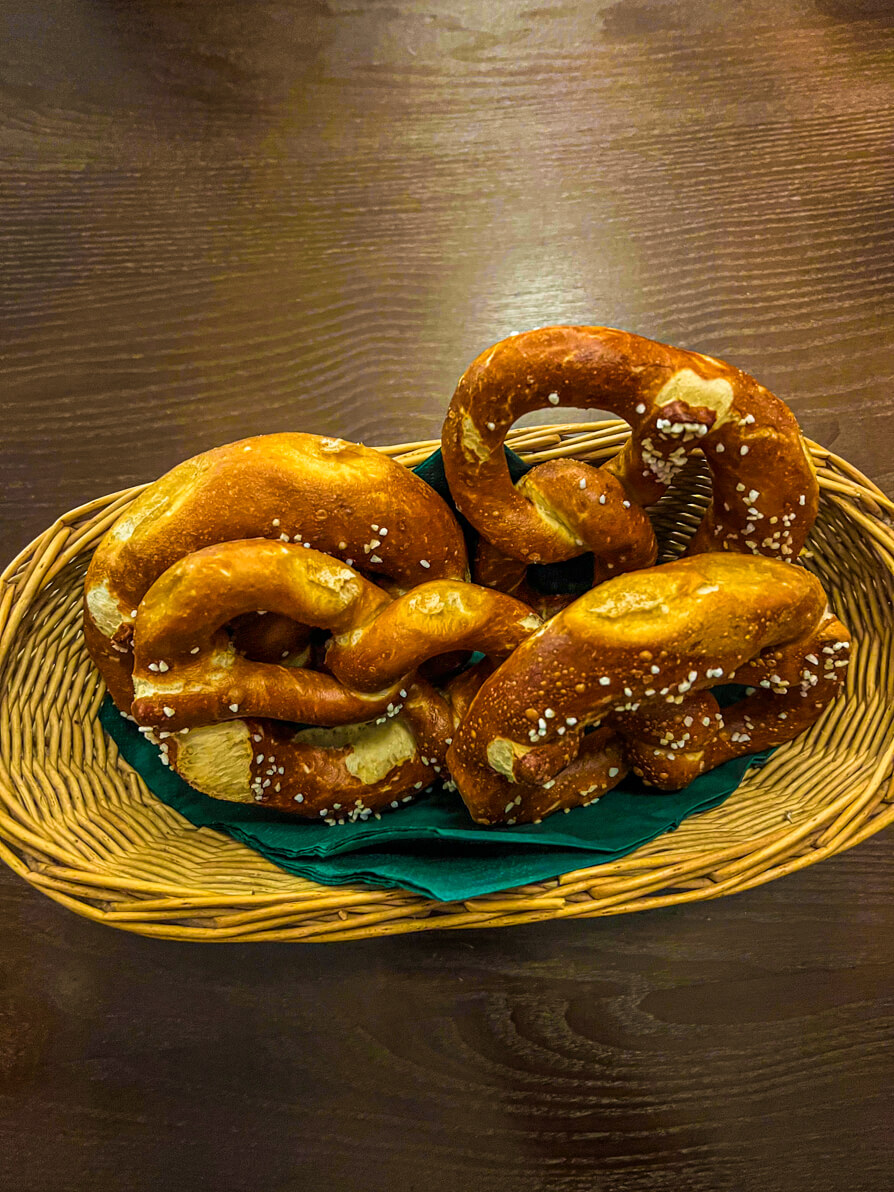 Bird's eye view of four pretzels on a green napkin in a woven basket on a brown table in Munich Germany