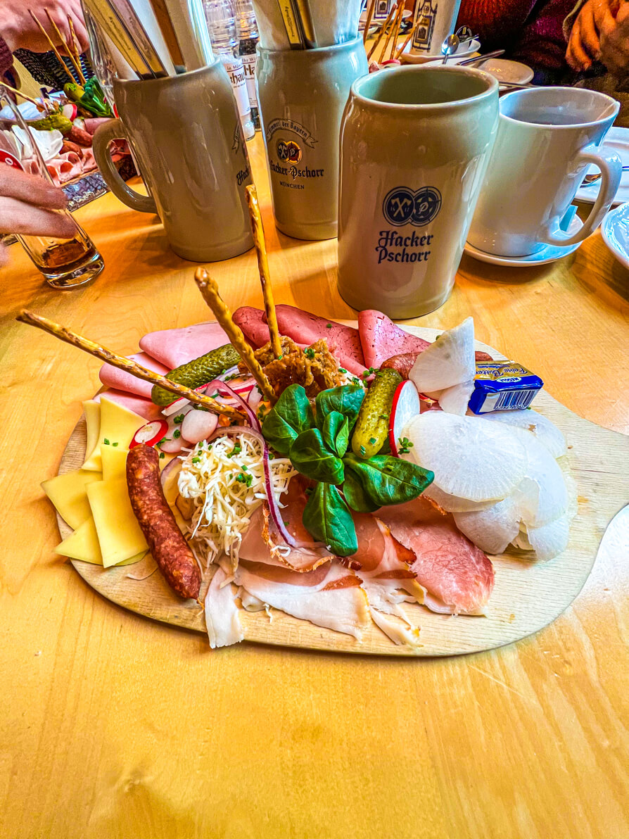Image of meat cheese and dip platter on wooden board with German dark beer behind on na wooden table in a braufhaus in Munich Germany on Food Tour