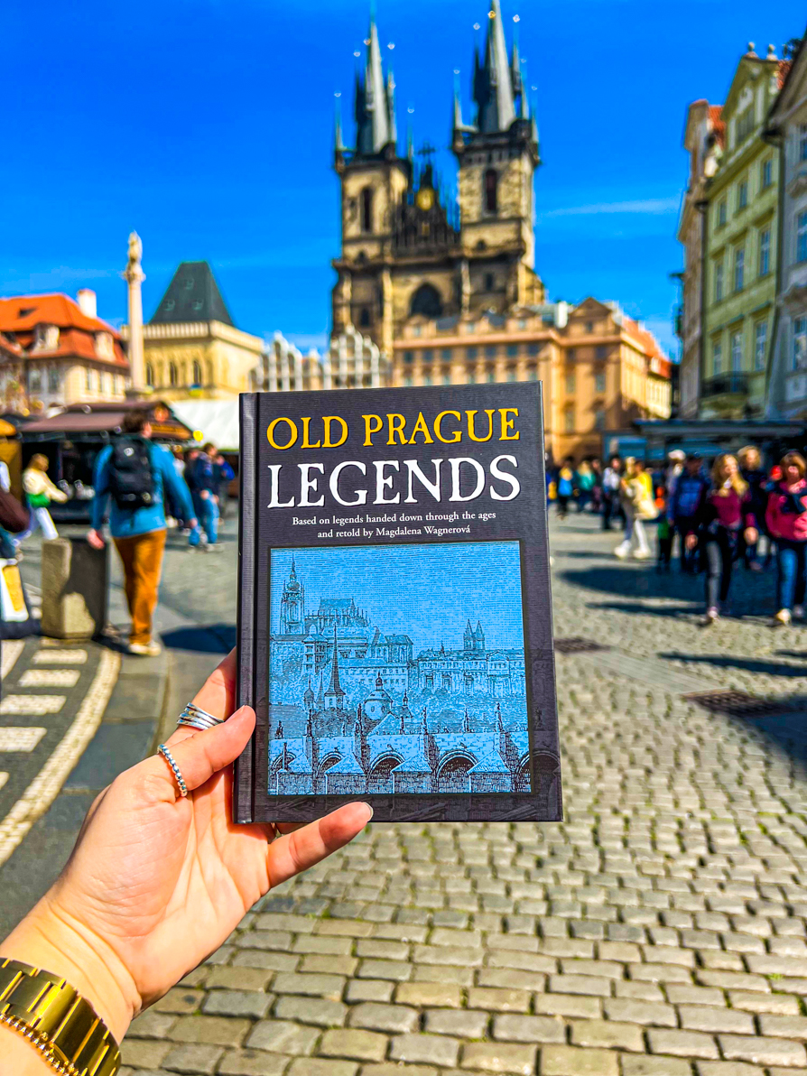 Shireen's left hand holding Old Prague Legends book in front of Old Town Square Prague