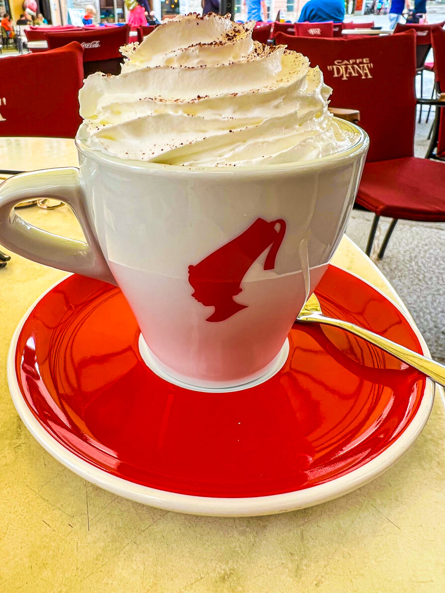 Close up image of coffee with cream in Croatia in a white mug on a red saucer.