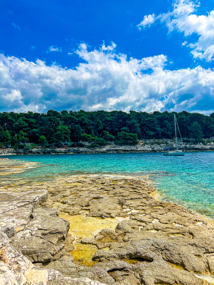Strand Pula also known as Gortana Cove in Stoja Pula Croatia from the right hand side rocks looking over water and woodlands with boat docked