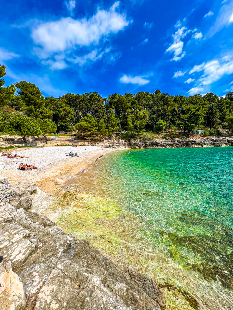 Strand Pula also known as Gortana Cove in Stoja Pula Croatia from the right hand side rocks looking over pebbles, water and woodlands