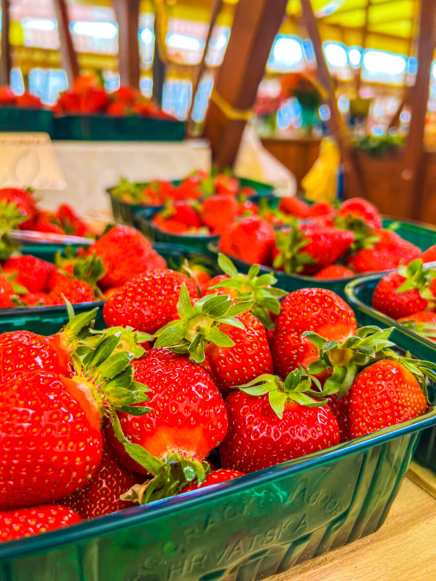 Close up of four punnets of strawberries in green plastic containers with canopies of Green Market in the background in Zadar Croatia