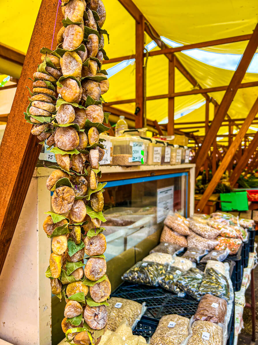 Dried figs hanging on the left of the stall with nuts and seeds in bags to the right with the green market canopies in the background in Zadar Croatia