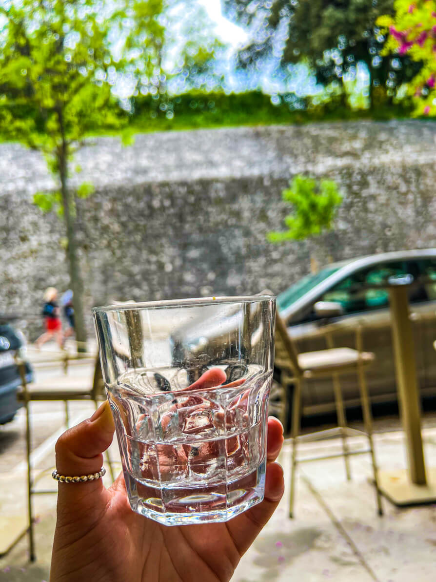 Image of Shireen's left hand holding up a glass of Maraschino to the Jelena Park walls in Zadar Croatia