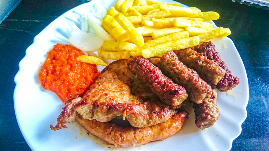 Image credit to Cosette from KarsTravels. Image of cevapcici, chips and Avjar on a white plate in Slovenia