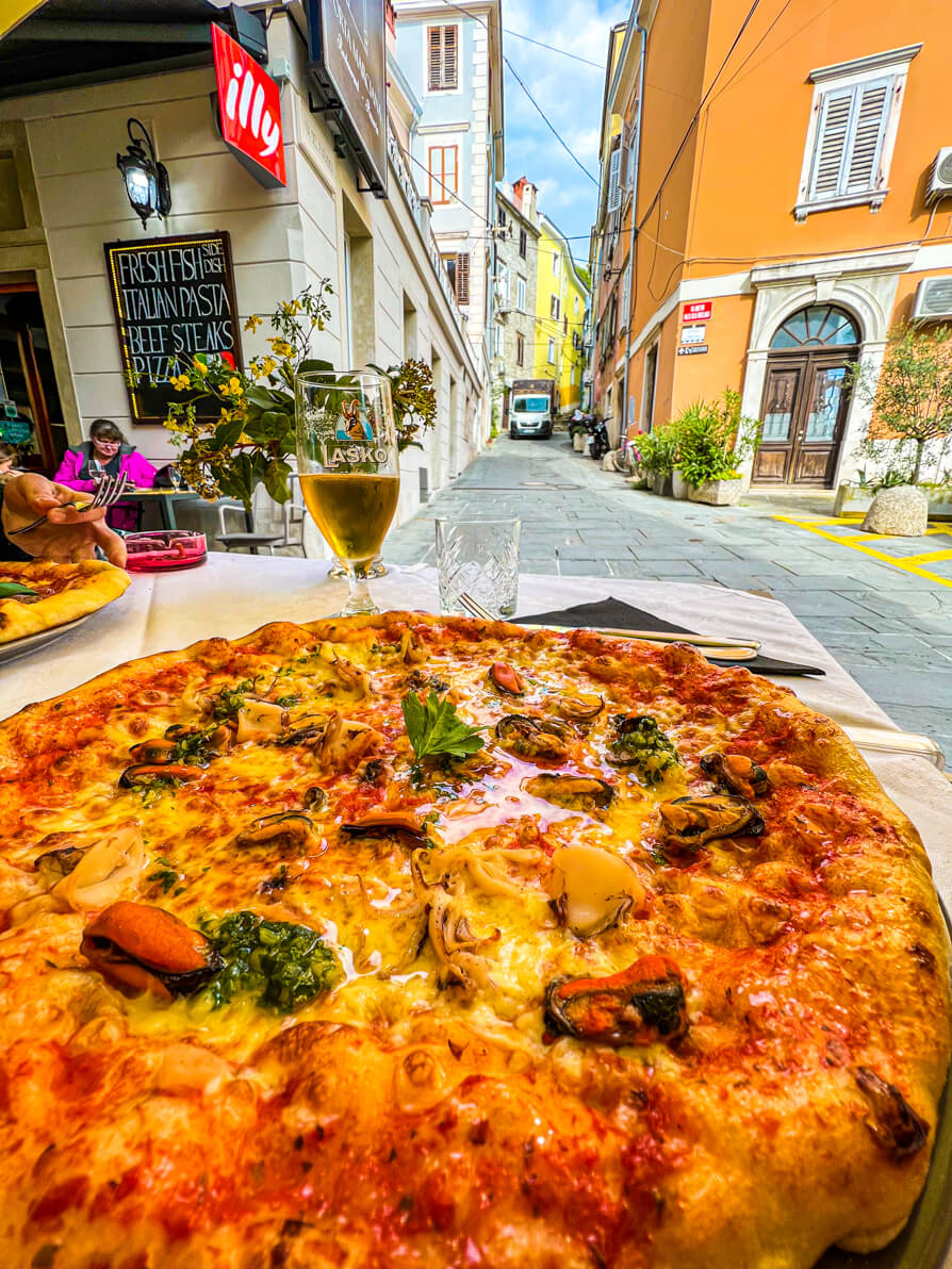 Image of seafood pizza in front with shop and lane in back in Piran Slovenia