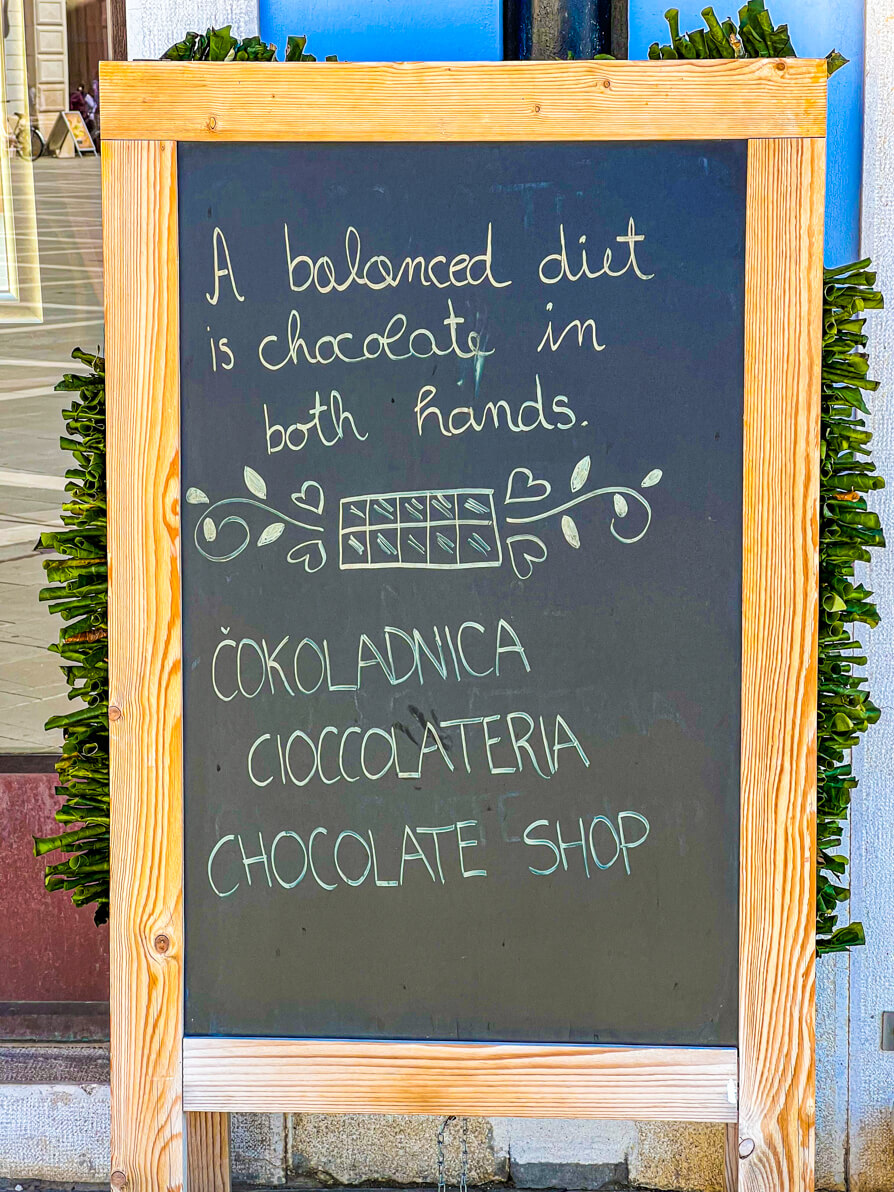 Image of sign outside Chocolate Shop. It reads 'A balanced diet is chocolate in both hands' and the shop name in Piran Slovenia