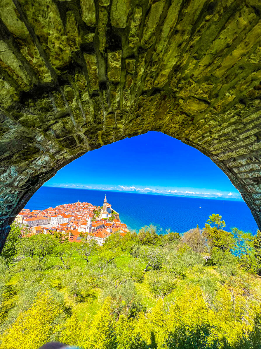 Image of Piran as seen through a hole in one of the ancient walls with blue sky and sea in background