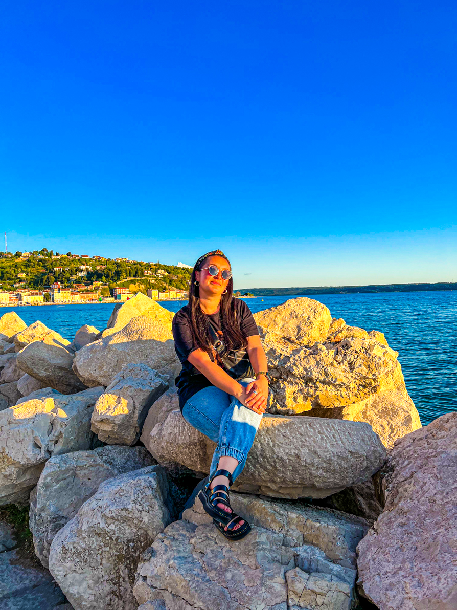 Image of Shireen smiling while sat on the rocks at sunset in Piran Slovenia