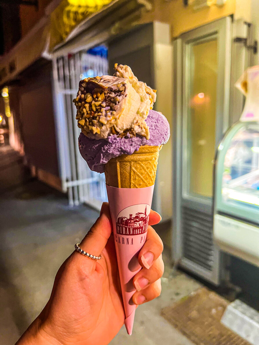 Image of Shireen's left hand holding up the half lavender, half kinder ice cream in Piran Slovenia
