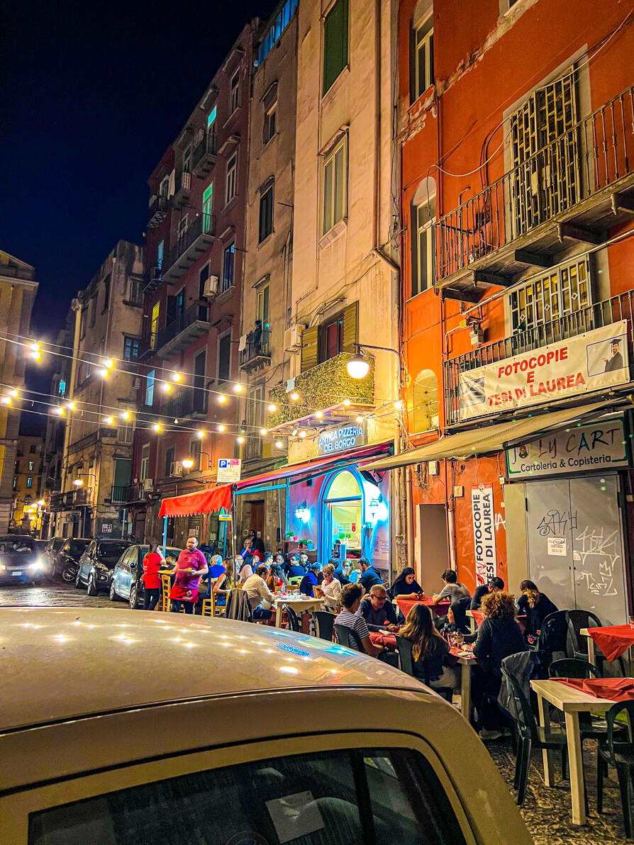 Exterior of Antica Pizzeria Del Borgo with busy tables at night in Naples Italy