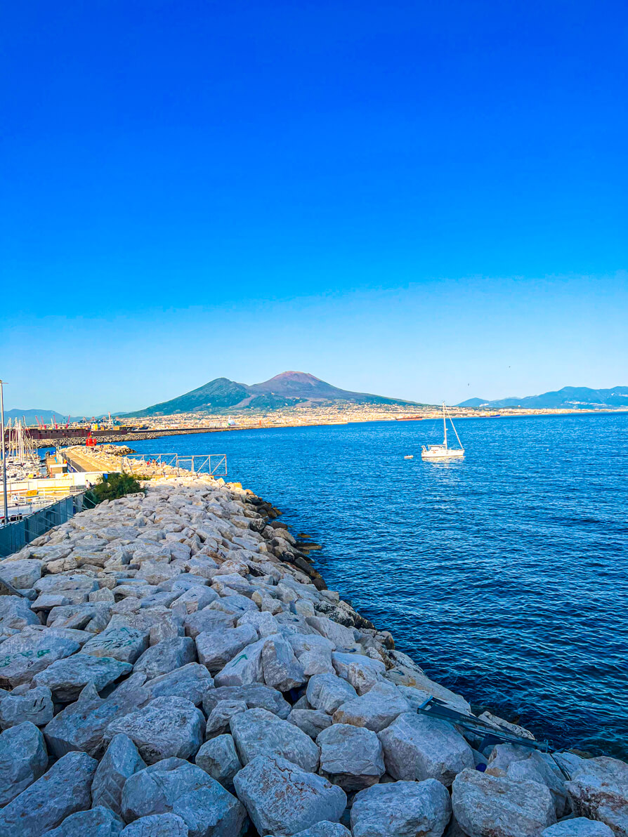 Image of Mt Vesuvius in background from the Lungomare view with rocks in forefront from Naples Port in Italy