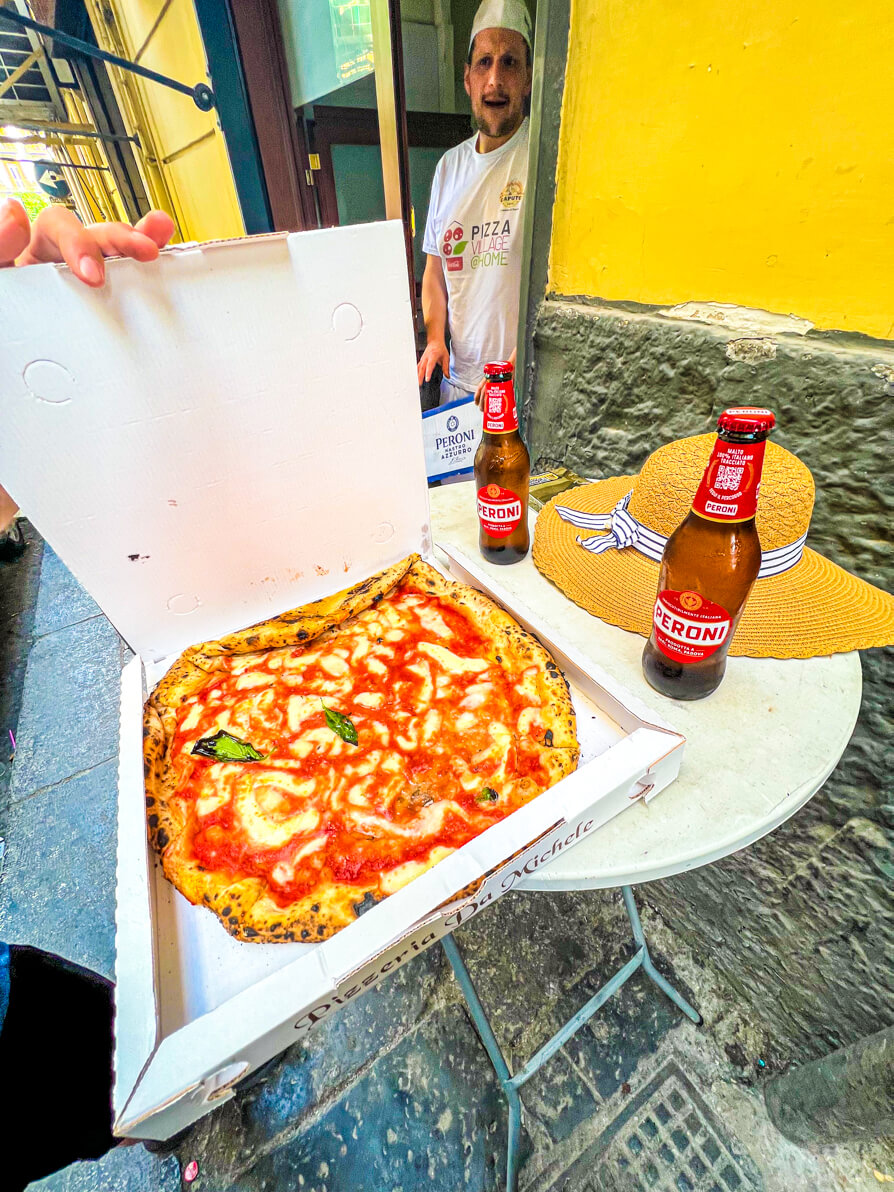 Image of Margarita pizza in a white pizza box with two peroni bottles and sun hat with chef in background at Pizzeria Michele in Naples Italy