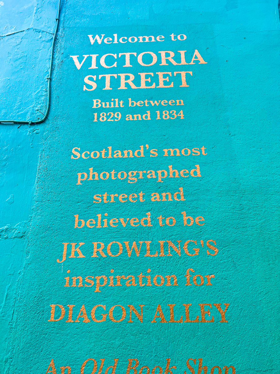 Gold writing on a green wall says 'Welcome to Victoria Street built between 1829 and 1834. Scotland's most photographed street and believed to be JK Rowling's inspiration for Diagon Alley. '