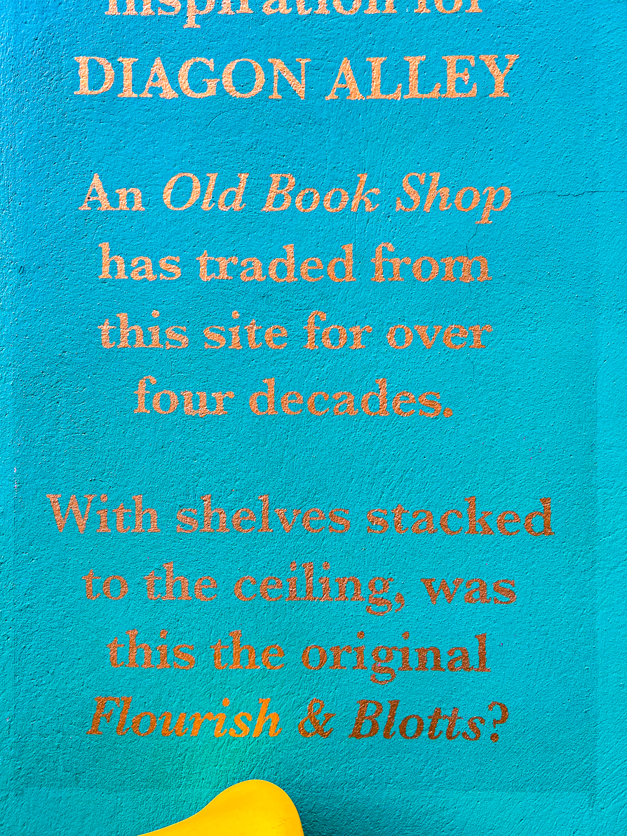 Gold writing on a green wall says  'An Old Book shop has traded from this site for over four decades. With shelves stacked to the ceiling, was this the original Flourish & Blotts?'