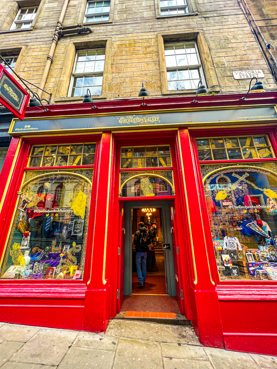 Exterior shot of Enchanted Galaxy shop on Victoria Street in Edinburgh. Building is red with gold writing and Harry Potter stuff on sale in the window.