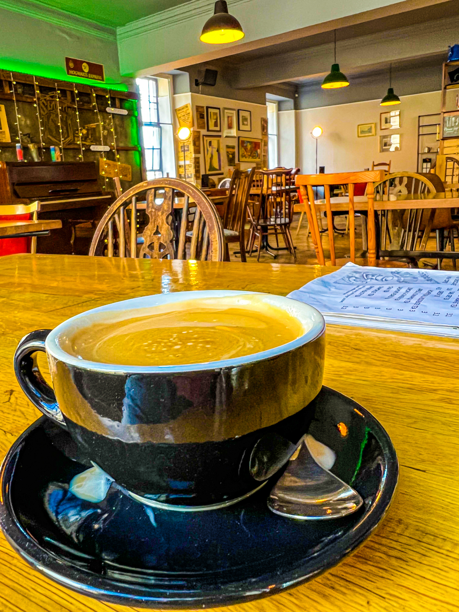 Coffee in black mug with Nicolsons Cafe Edinburgh in background