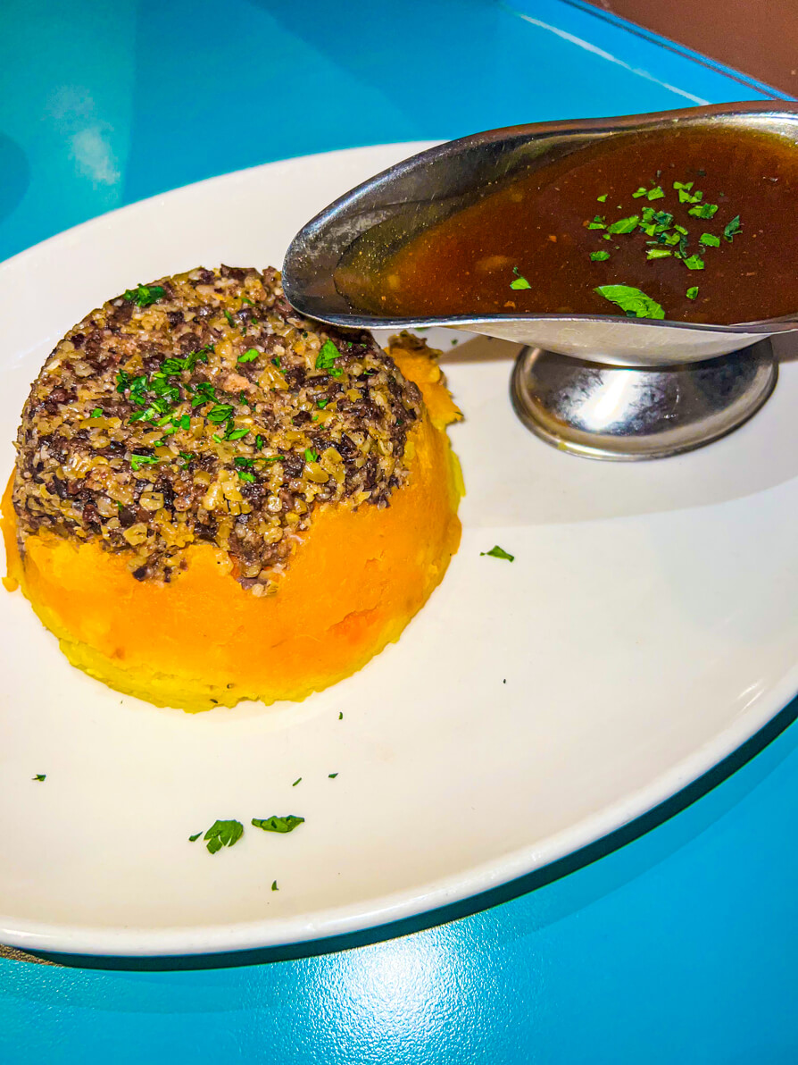 Image of Haggis Neeps and Tatties on a white plate with a silver gravy boat of gravy in Scotland