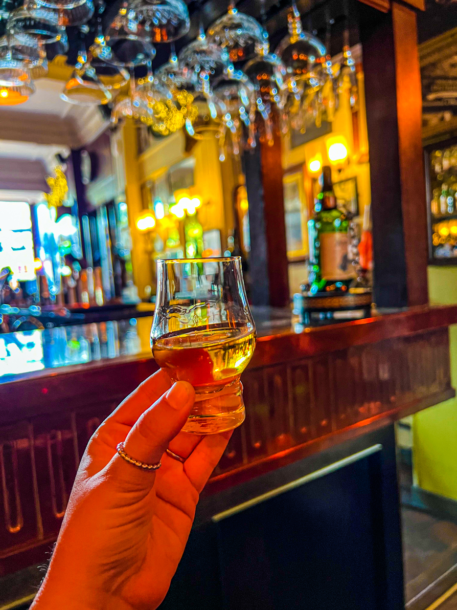 Image of Shireen's left hand holding up a drum of Whiskey in a pub in Edinburgh Scotland