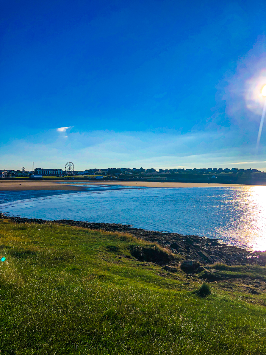 Image of Barry Island from point looking over blue ocean and blue sky with green grass in front in Barry Wales