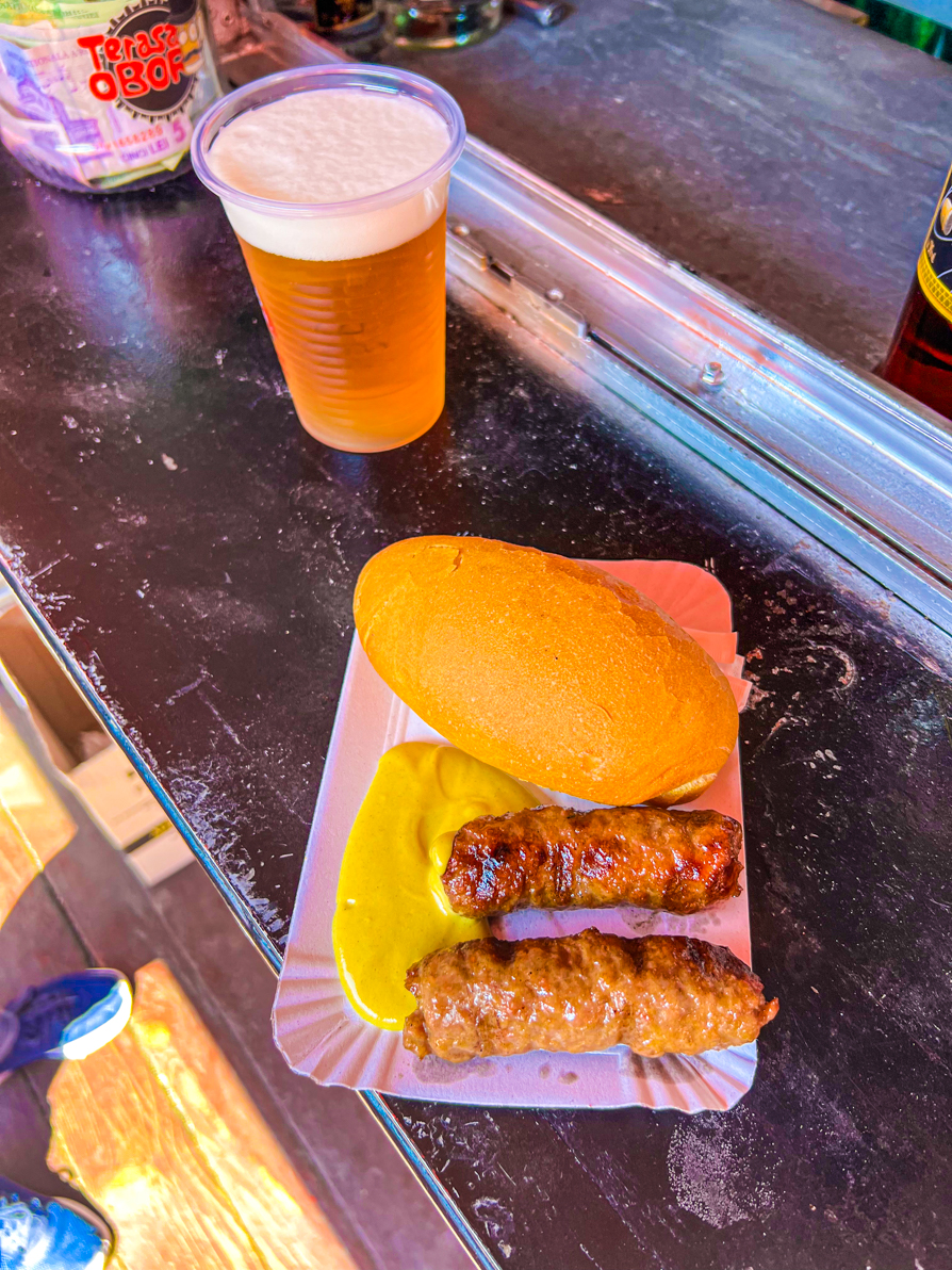 Bird's eye view of two mici with mustard and bread and beer on the side on a marble counter in Bucharest