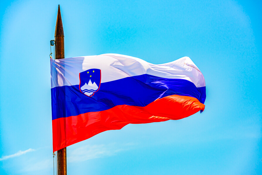 Image of Slovenia Flag on a pole with blue sky background. Credit to unsplash.
