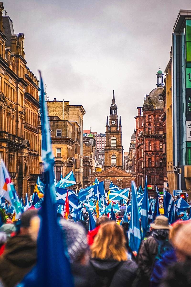 Image credit to Unsplash. Image of Edinburgh streets with dozens of people holding up Scottish flags