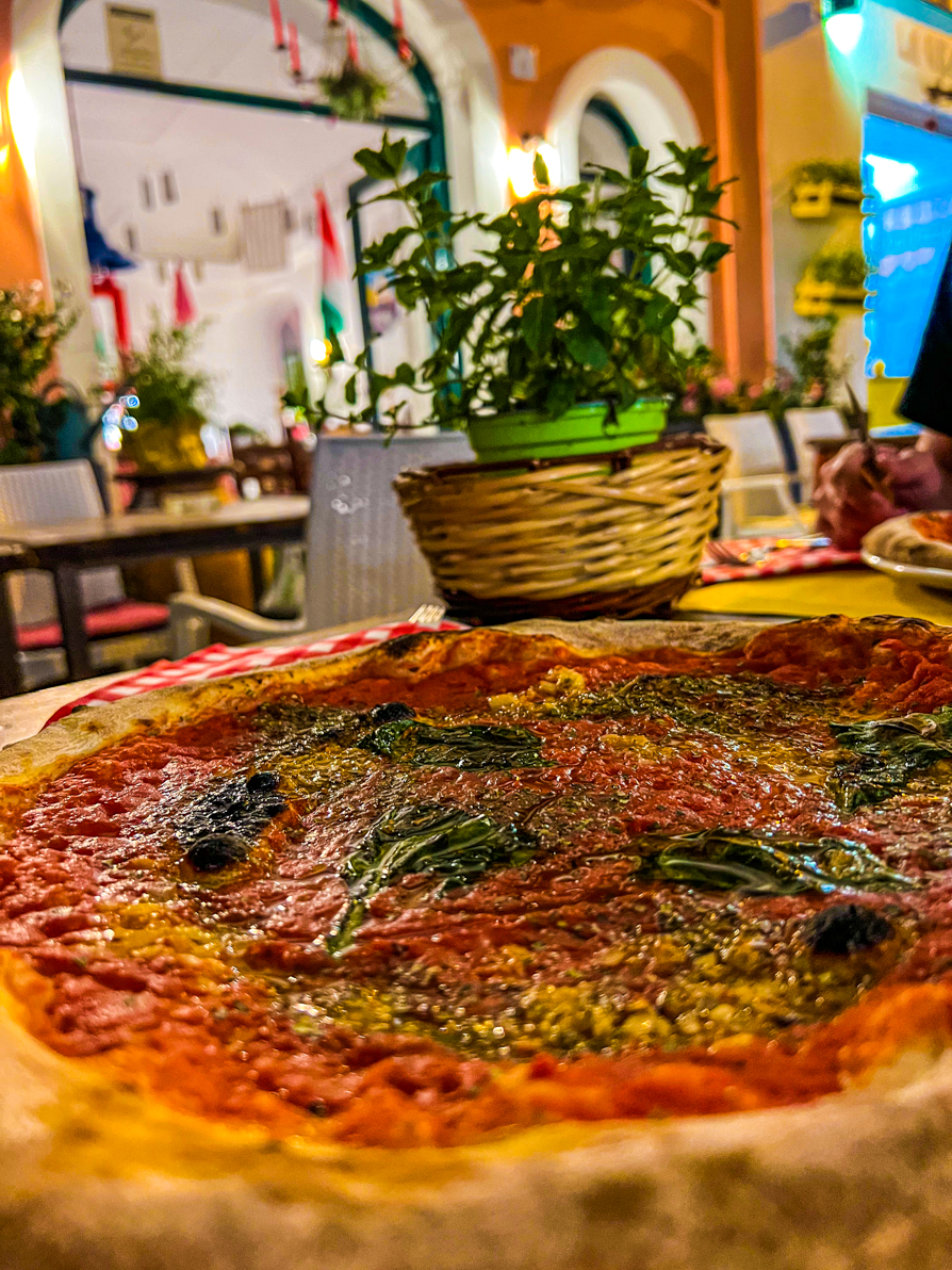 Pizza Marinara up close with plant and restaurant in background in Italy