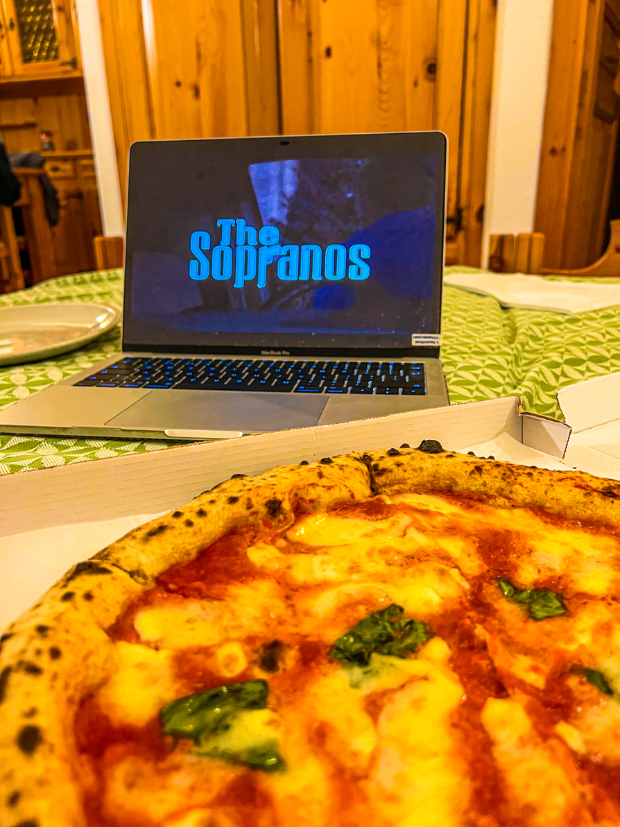 Image of pizza in white box in front of laptop showing The Sopranos opening credits